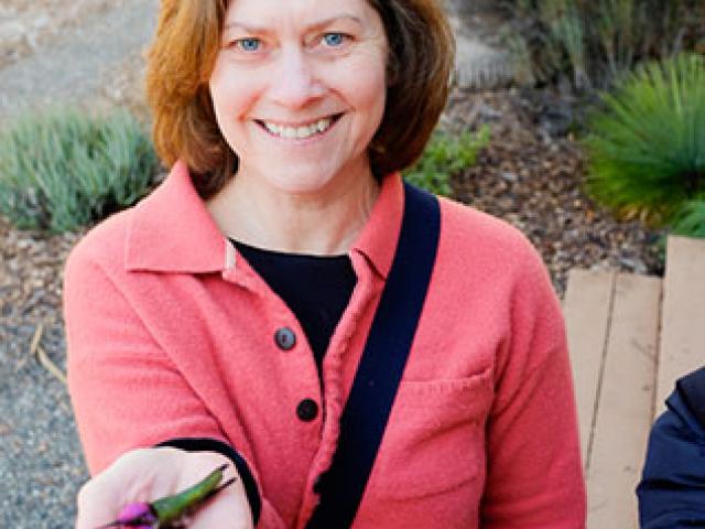 A smiling woman holding a hummingbird in her outstreched hand